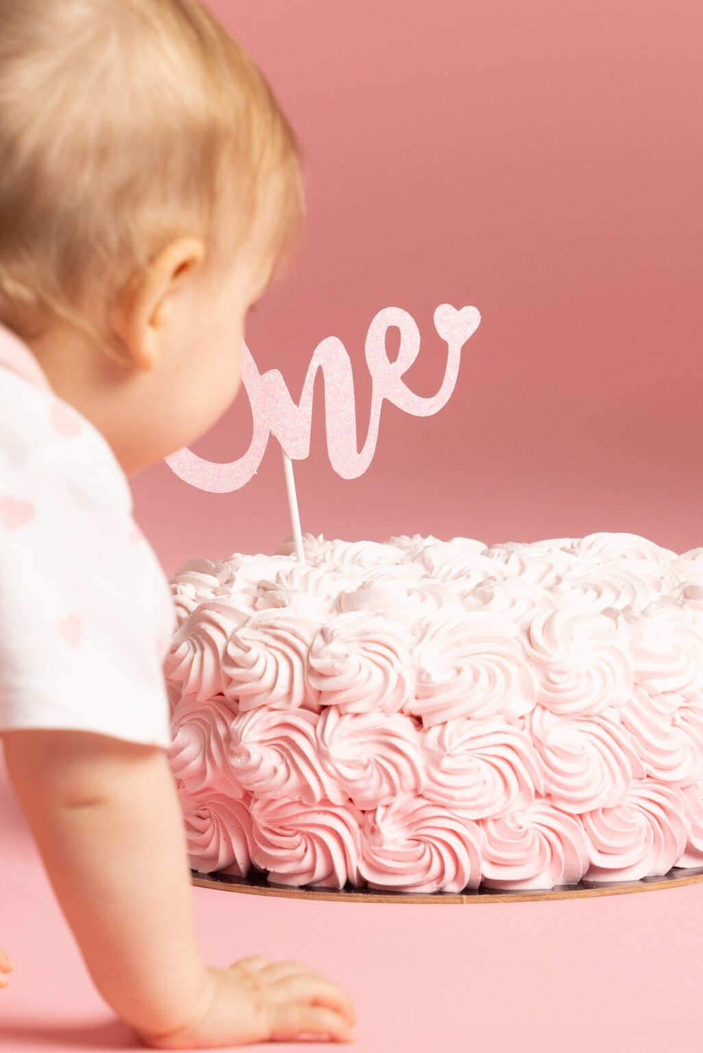 Bebè che gattona verso la Smash Cake con rose di panna rosa e topper “One”