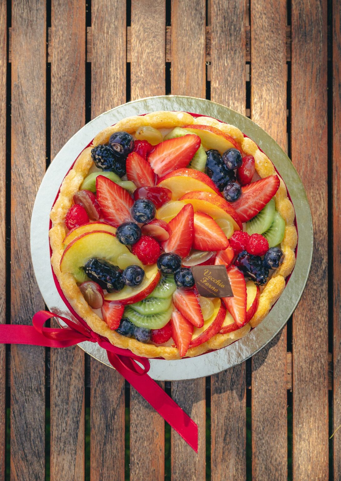 Torta Charlotte vista dall’alto con frutta fresca e nastro rosso